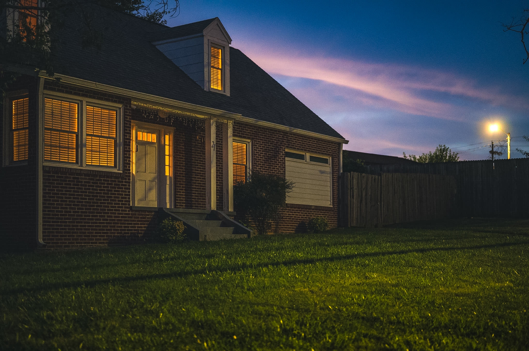 A brick house at dusk with its porch light on