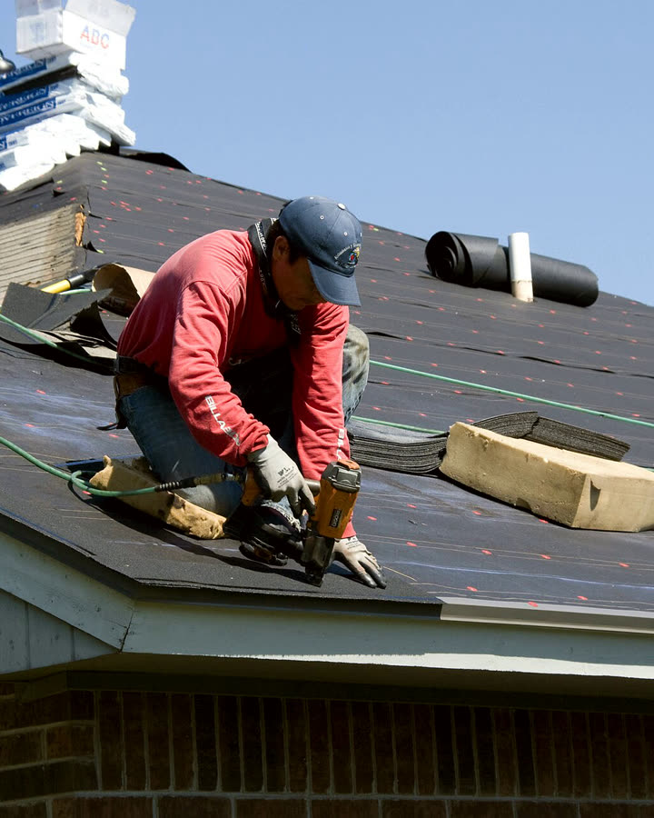 A roofer nailing shingles on a pitched roof